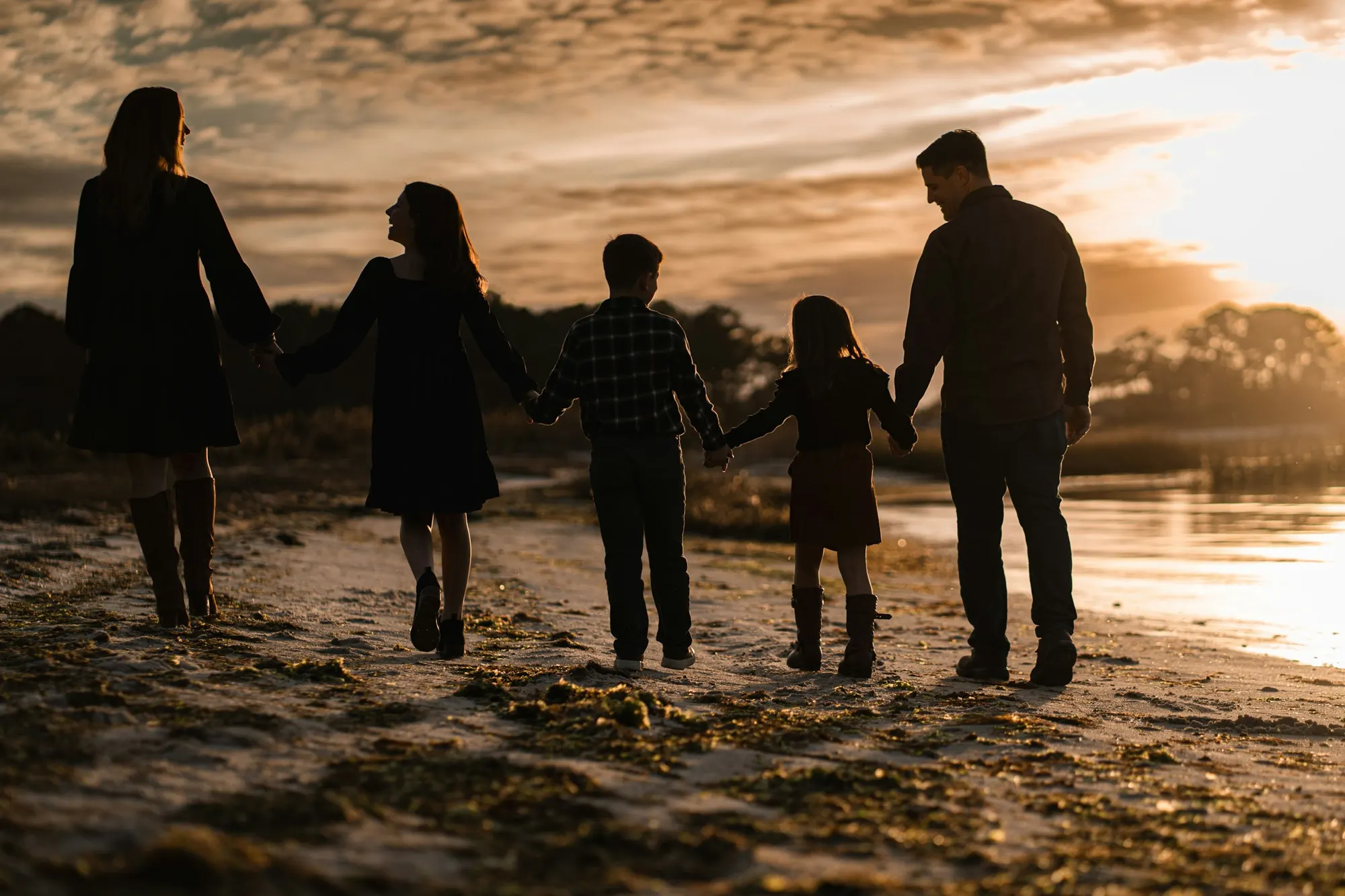 Une famille marchant sur une plage au coucher du soleil, à contre-jour